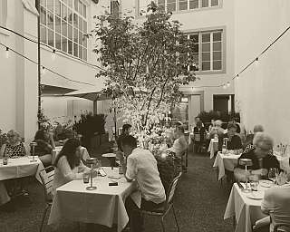Menschen sitzen an gedeckten Tischen im Innenhof eines Restaurants mit Baum und Lichterketten