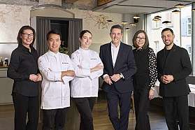 Sechs Personen, darunter zwei Köche in weißen Jacken, stehen in einem Restaurant